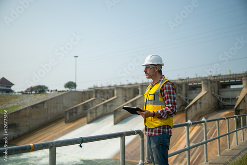 Fotografi Portrait of engineer wearing yellow vest and white helmet with tablet Working day on a water dam with a hydroelectric power plant