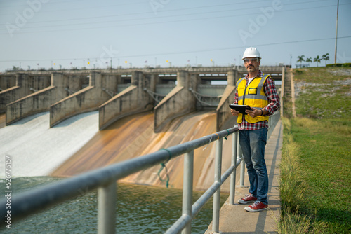 Portrait of engineer wearing yellow vest and white helmet with tablet Working day on a water dam with a hydroelectric power plant. Renewable energy systems, Sustainable energy concept