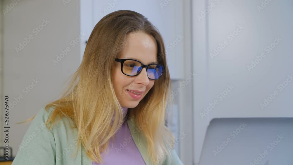 White woman working on laptop computer. Cheerful blonde female doing distant work online on notebook pc. Adult Ukrainian person in glasses works on laptop at home with a smile in 4k stock video clip