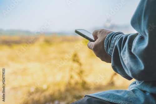Hand of Asian elderly man farmer use cellphone for business to plan farming in meadow. Male farmers consult with landowners to cultivate crops in field. Farm and agricultural technology and business.