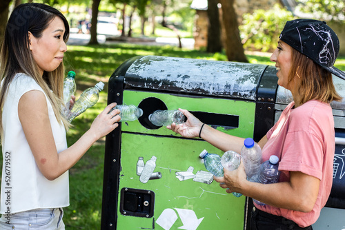 Foto Smiling young friends women picking up and throwing plastic bottles in a recycli