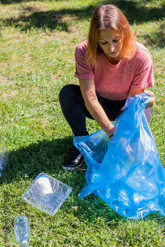 Red hair young woman collecting plastic bottles in a public park. Environmental awareness and desire to recycle