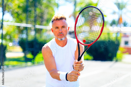 mature handsome man playing tennis on tennis court at sunny day © yurakrasil