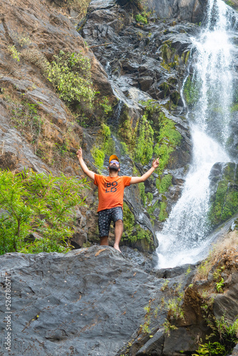 Tourist standing in front of vibhooti water falls showing hands to sky