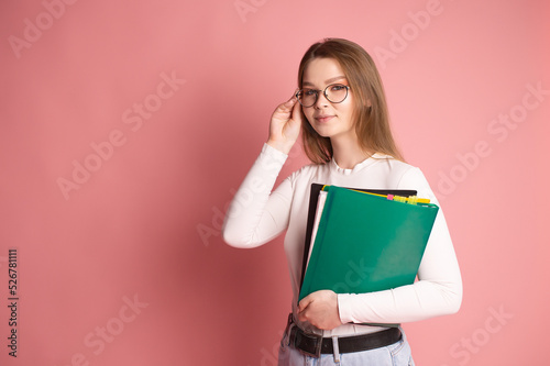 Cute student with glasses holds colorful folders on a pink background