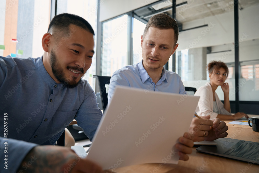 Male colleagues reviewing documents together while sitting in open office Male colleagues reviewing documents together while sitting in open office