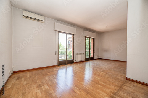 Empty living room of a residential house with oak parquet floor, two large aluminum and glass balconies and air conditioner on the wall