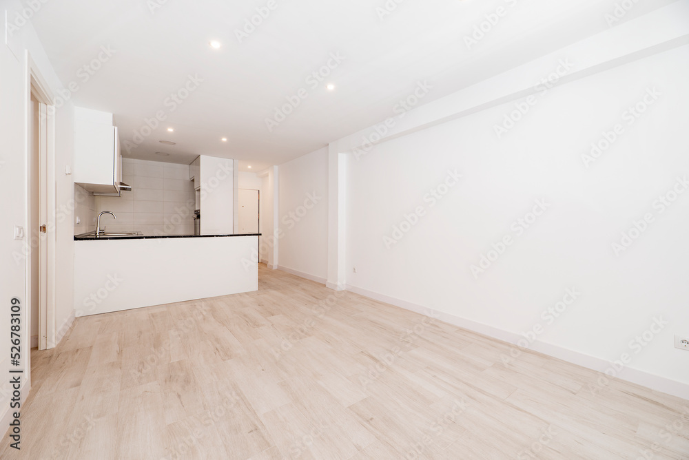 Fototapeta premium empty room has light wood floor, plain white painted wall, island with black stone countertop and open kitchen