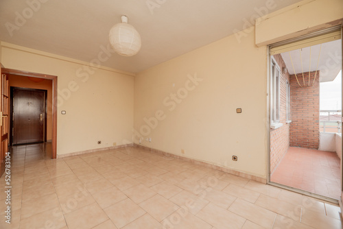 empty room has square tile stoneware floor  cream painted wall with gotelet  access to a terrace with clay floors and reddish wooden door with glass window