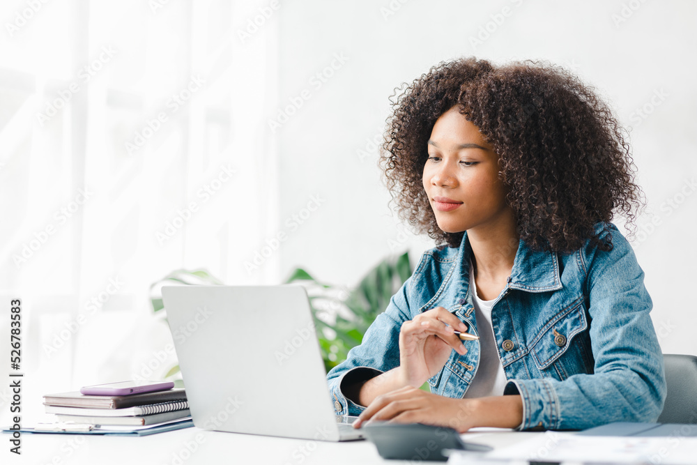 American teenage woman sitting in white office with laptop, she is a student studying online with laptop at home, university student studying online, online web education concept. American teenage woman sitting in white office with laptop, she is a student studying online with laptop at home, university student studying online, online web education concept.