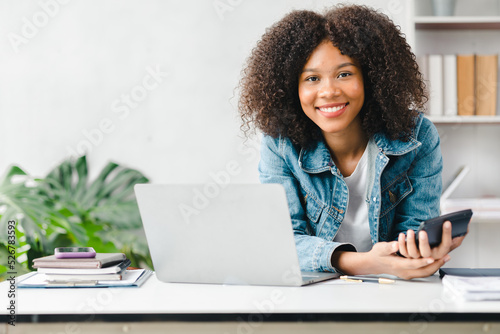 American teenage woman sitting in white office with laptop, she is a student studying online with laptop at home, university student studying online, online web education concept.