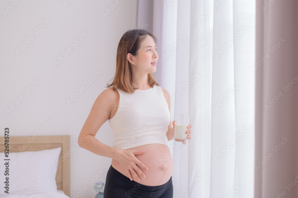 Young Asian woman standing in bedroom holding a glass of fresh milk Young Asian woman standing in bedroom holding a glass of fresh milk