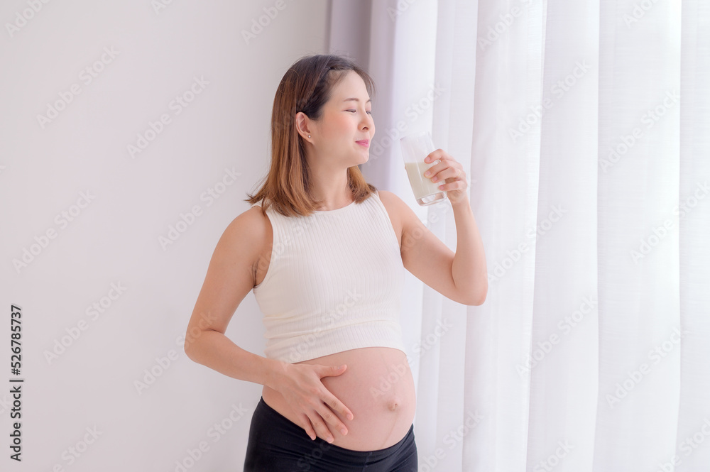 Young Asian woman standing in bedroom holding a glass of fresh milk Young Asian woman standing in bedroom holding a glass of fresh milk