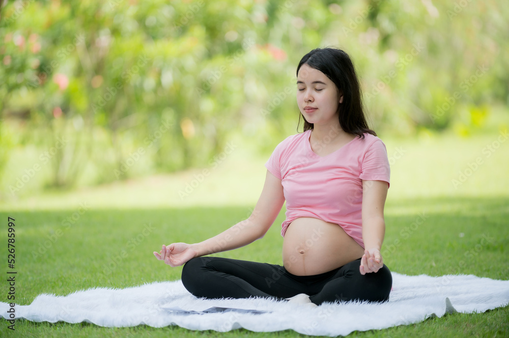 A pregnant Asian woman relaxes with yoga stretching exercises in the park for the health of the mother and the unborn child A pregnant Asian woman relaxes with yoga stretching exercises in the park for the health of the mother and the unborn child