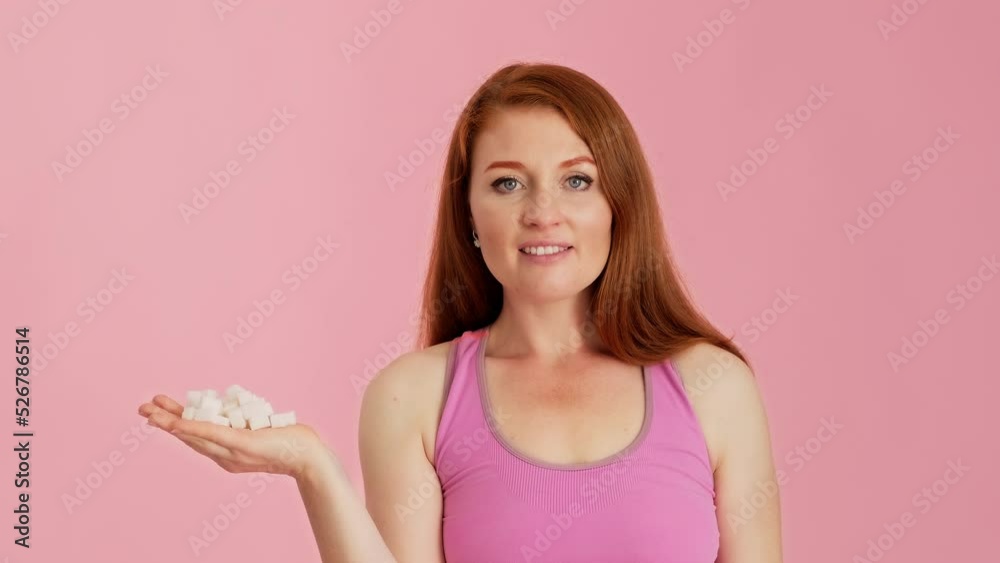 Woman is holding handful of sugar cubes at pink background. Unhealthy eating concept. Female in T-shirt holding pile of sugar cubes and looking at camera. Pure carbohydrates. 4K, UHD Woman is holding handful of sugar cubes at pink background. Unhealthy eating concept. Female in T-shirt holding pile of sugar cubes and looking at camera. Pure carbohydrates. 4K, UHD