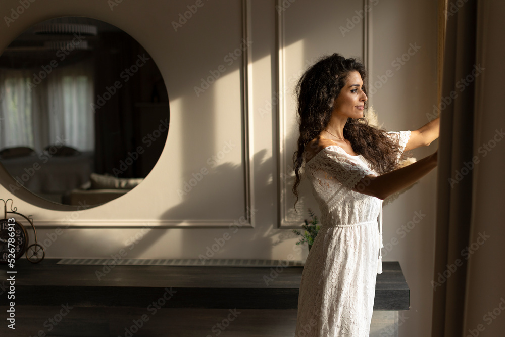 Young curly hair woman standing by the window in the room