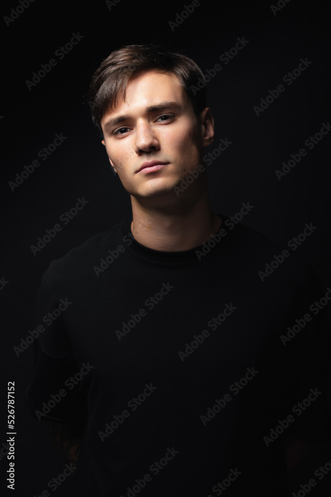 A guy of model appearance in black clothes poses on a black studio background. Male fashion portrait
