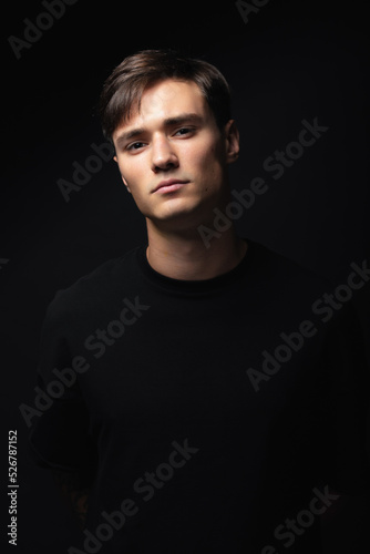 A guy of model appearance in black clothes poses on a black studio background. Male fashion portrait