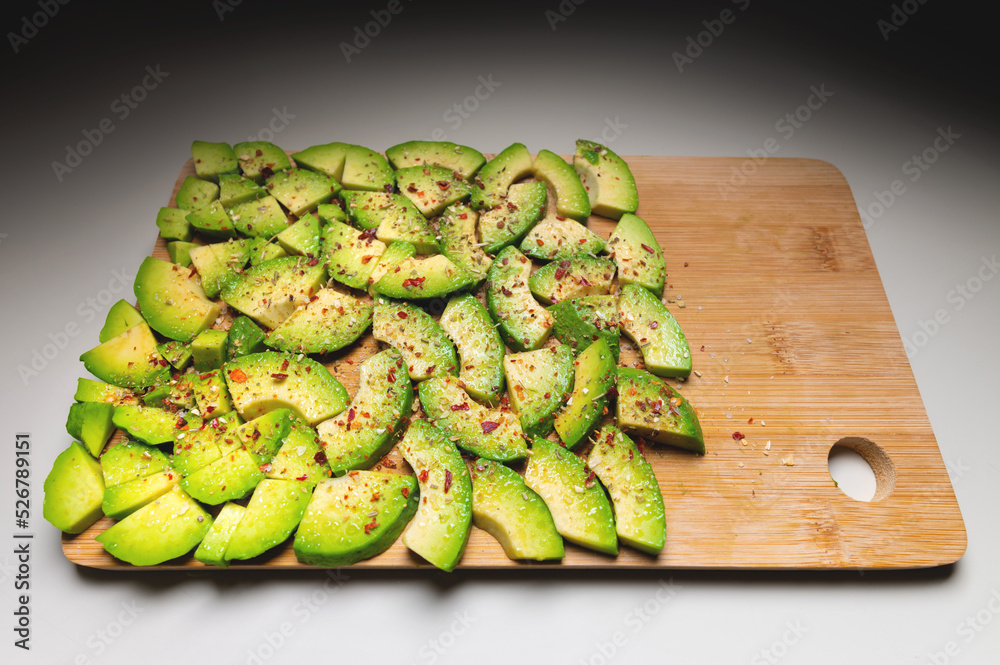 Avocado slices on a wooden textured background sprinkled with spices, bright accent. View from above