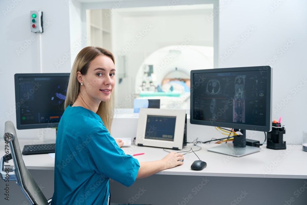 Woman in medical clothes sits half-turned table and looks into lens Woman in medical clothes sits half-turned table and looks into lens