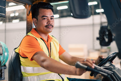Portrait of male Asian driver driving forklift to shipping delivery in the warehouse distribution. import export logistic career, worker working at industrial factory. © winnievinzence
