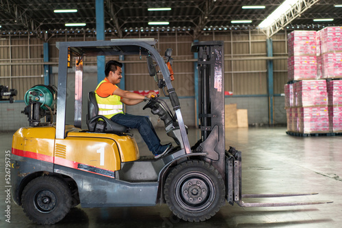 Asian male driver driving forklift to shipping delivery product in the warehouse distribution. import export logistic career, worker working at industrial factory. © winnievinzence