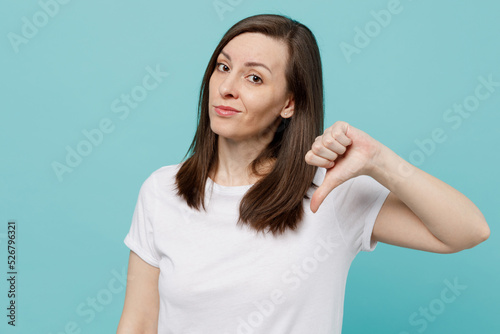 Young dissatisfied unhappy sad caucasian woman 20s she wear white t-shirt show thumb down dislike gesture isolated on plain pastel light blue cyan background studio portrait. People lifestyle concept.