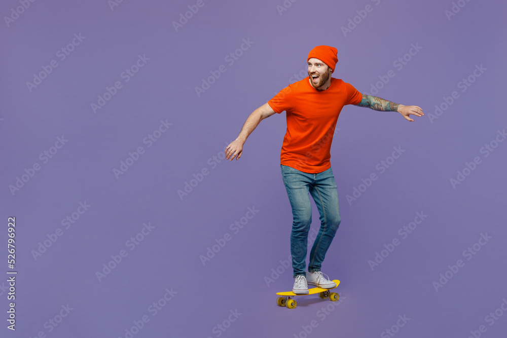 Full body side view amazed happy young european man 20s he wears red hat t-shirt rides pennyboard skateboard isolated on plain pastel light purple background studio portrait. People lifestyle concept. Full body side view amazed happy young european man 20s he wears red hat t-shirt rides pennyboard skateboard isolated on plain pastel light purple background studio portrait. People lifestyle concept.