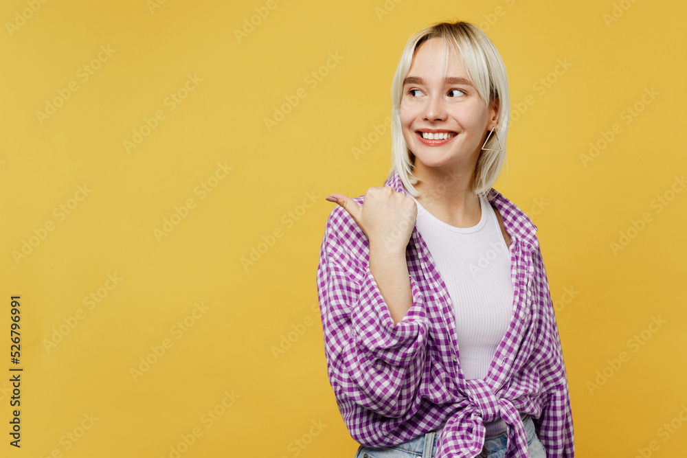 Young blonde woman 20s she wear pink tied shirt white t-shirt pointing thumb finger aside indicate on workspace area copy space mock up isolated on plain yellow background. People lifestyle concept. Young blonde woman 20s she wear pink tied shirt white t-shirt pointing thumb finger aside indicate on workspace area copy space mock up isolated on plain yellow background. People lifestyle concept.