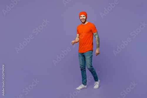 Full body young smiling happy european man 20s he wear red hat t-shirt hold walking going look camera isolated on plain pastel light purple background studio portrait. Tattoo translates life is fight.