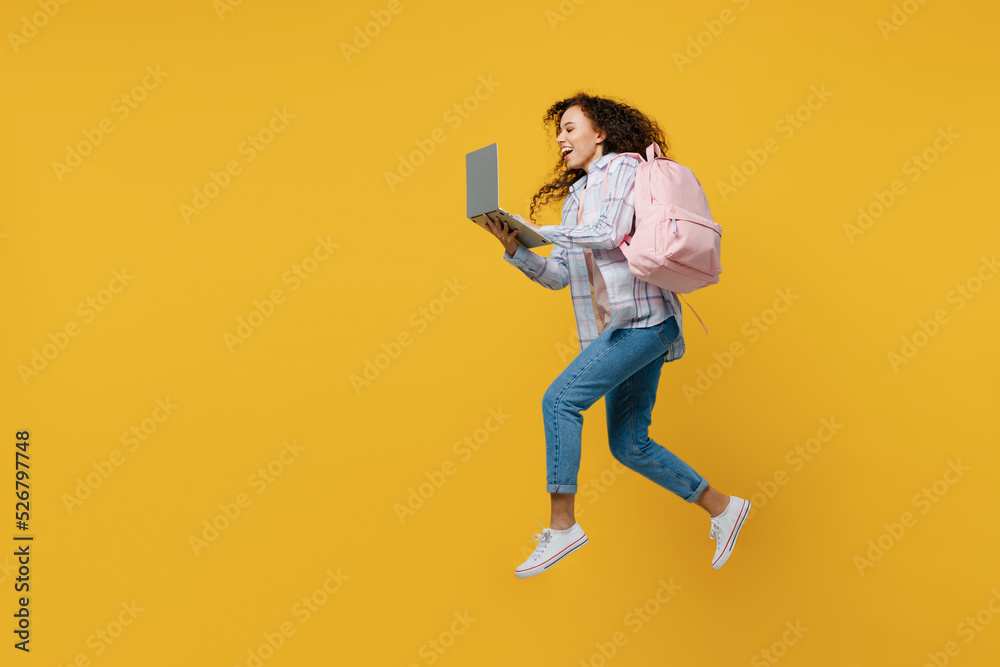 Full size side view young black teen girl student she wear casual clothes backpack bag jump high hold use laptop pc computer isolated on plain yellow background. High school university college concept Full size side view young black teen girl student she wear casual clothes backpack bag jump high hold use laptop pc computer isolated on plain yellow background. High school university college concept