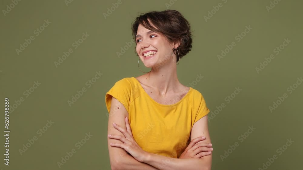Young smiling cheerful fun european woman 20s she wearing yellow t-shirt hold hands crossed folded look camera aside isolated on plain pastel green background studio portrait. People lifestyle concept