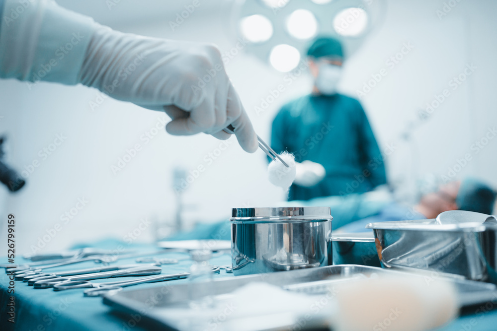 Close up surgeon doctor's hand with hygiene glove taking sterile surgical instrument tool, equipment in operating room patient in background for surgery. Hospital, medical healthcare emergency concept Close up surgeon doctor's hand with hygiene glove taking sterile surgical instrument tool, equipment in operating room patient in background for surgery. Hospital, medical healthcare emergency concept