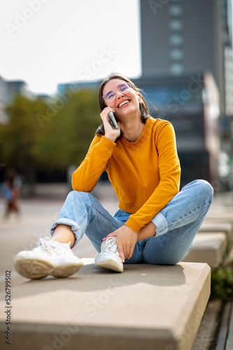 Cheerful woman talking on mobile phone sitting on bench outside in the city