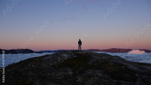 Person standing on cliff overlooking icebergs in Greenland