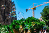 In-Focus Soap Bubbles, Against An Out-Of-Focus Background Of Palm Trees, Yellow Building Crane And The Sagrada Familia In Barcelona, Spain.