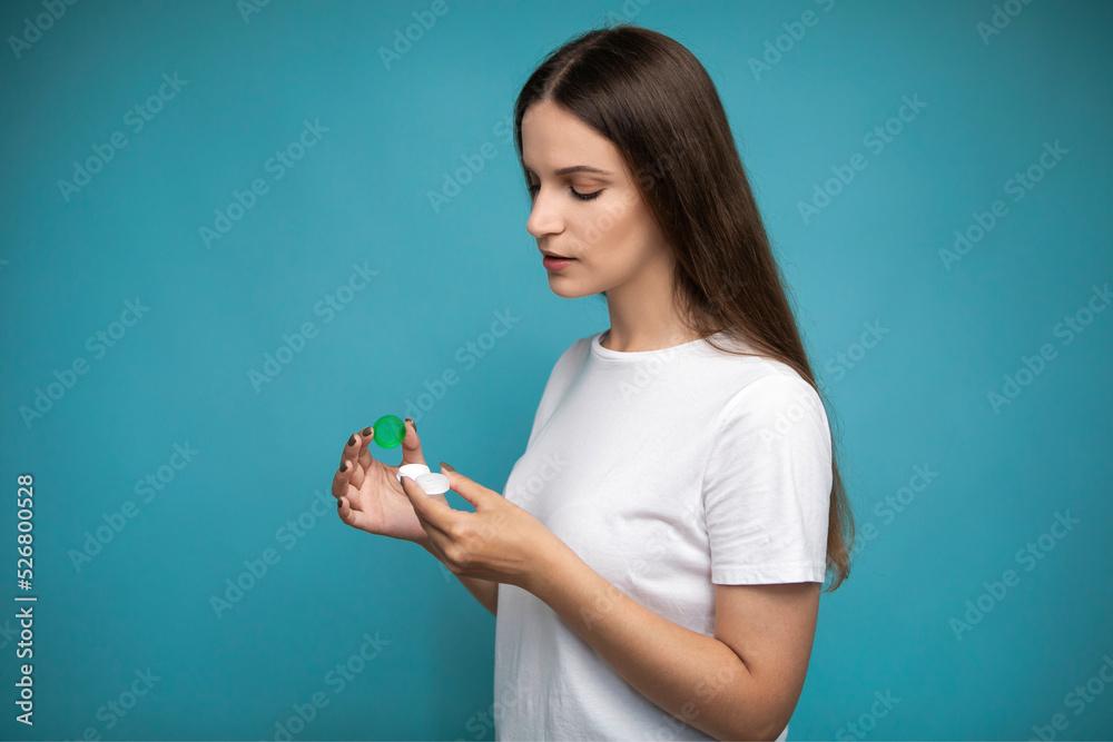 Young woman with contact lenses container on blue background Young woman with contact lenses container on blue background