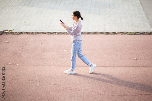 Young woman walking outside wearing earphone and using mobile phone