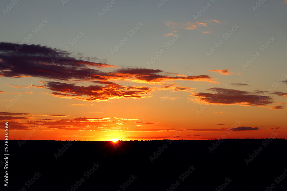  Summer landscape: sunset sky with golden clouds over the field with the setting sun