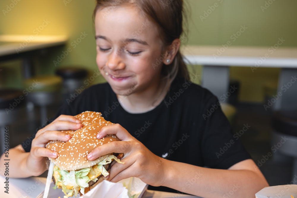 A little girl eats an appetizing burger, close-up. A little girl eats an appetizing burger, close-up.