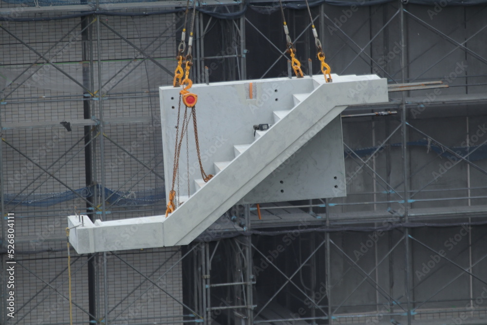 ビル建設現場で大型クレーンによる階段ユニット吊り上げ作業