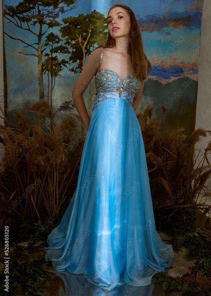an elegant woman in a long blue shiny dress stands in a fabulous location.
