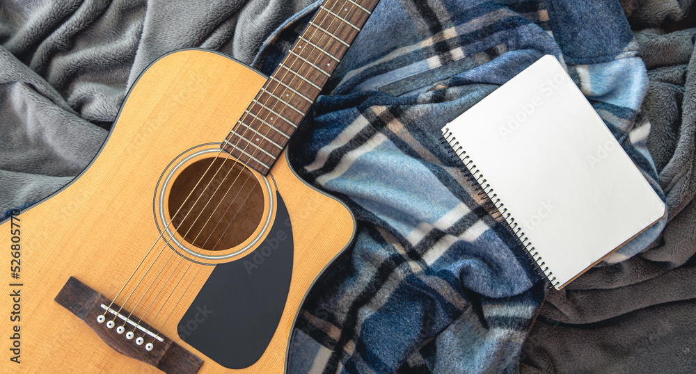 Fototapeta premium Acoustic guitar and notepad on a plaid background, top view.