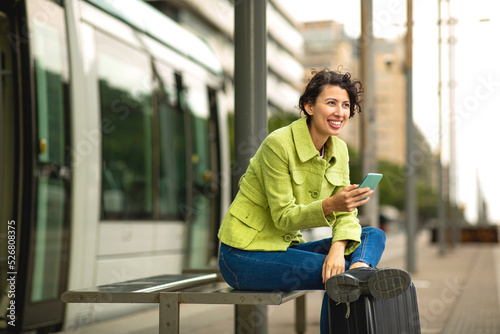 Smiling woman waiting at bus stop with mobile phone photo