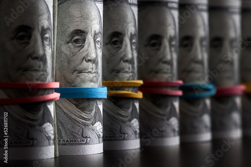 A row of rolled hundred dollar bills with rubber bands on dark background photo