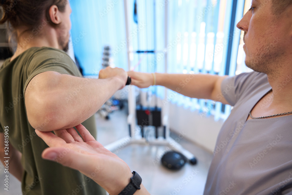 Obraz premium Instructor helps the patient in performing exercises on power simulator