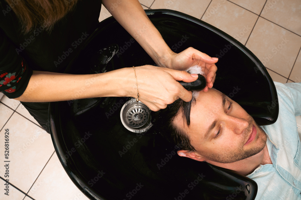 Fototapeta premium Hair salon master washing client hair at barber shop. Male client getting haircut by hairdresser. Hair care, beauty industry, barber concept