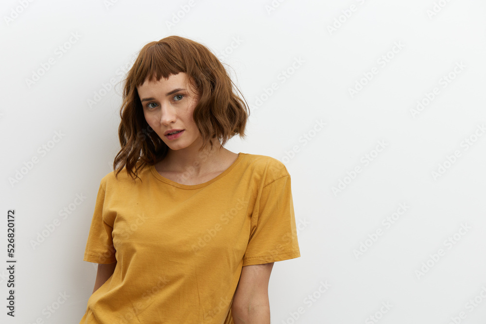 Fototapeta premium a sweet, beautiful, romantic woman in a yellow T-shirt poses on a white background, smiling pleasantly looking at the camera. Horizontal photo with an empty space for inserting an advertising layout