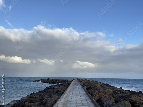 Cobblestone walkway netween rocks on the shore under blue cloudy sky photo