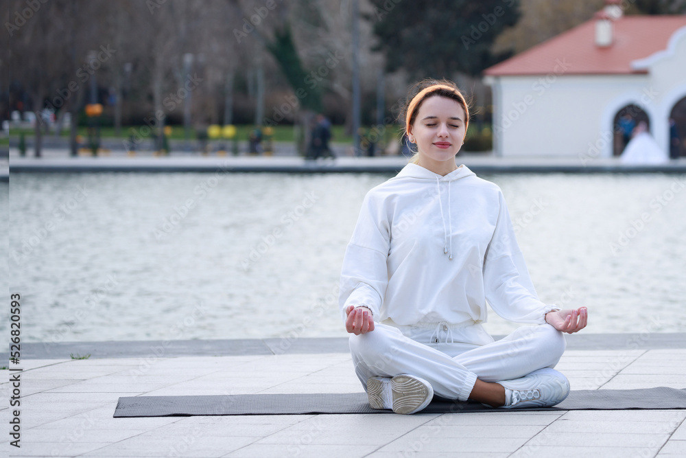 Young beautiful girl doing meditation on yoga mat at the park